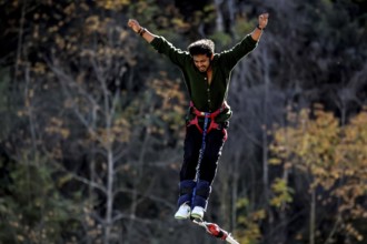 Person with arms spread out bungee jumping in front of autumn landscape, Queenstown, Otago, New