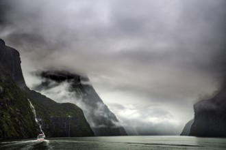Majestic fjord with waterfalls and a boat in thick fog