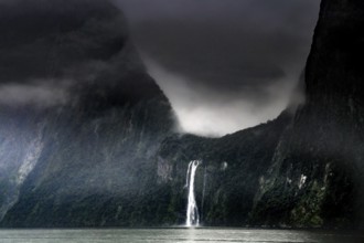 Dramatic sky over a waterfall in Milford Sound surrounded by misty mountains, zero
