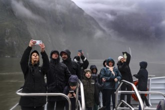 Group of passengers take pictures of the misty landscape from a cruise ship, Milford Sound, New