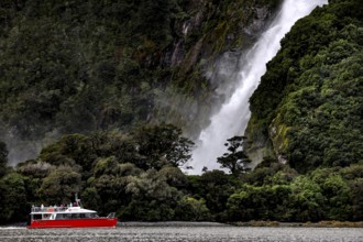 Boat sails past an impressive waterfall surrounded by lush vegetation, Milford Sound, New Zealand