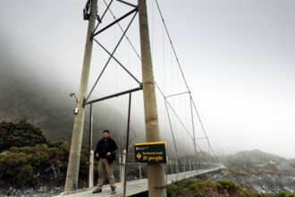 A man explores a high bridge in thick clouds of fog, Mt Cook, Hocker Valley Track, New Zealand
