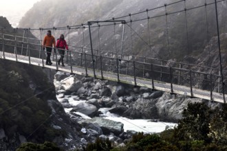 Hikers crossing a suspension bridge in a misty mountain landscape, Mt Cook, Hocker Valley Track,