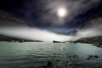 Calm glacial lake in moonlight surrounded by dramatic mountain peaks, Mount Cook, New Zealand