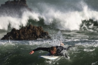 Surfer fights with big waves on the wild coast of Piha Beach, Piha Beach, New Zealand