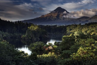 Mount Taranaki rises majestically above Lake Mangamahoe surrounded by lush greenery, New Zealand,