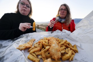 Two woman enjoying fish 'n' chips on Kaikoura beach, Kaikoura, Canterbury, New Zealand