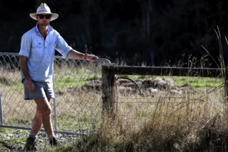 Man wearing sunscreen clothing stands next to a pasture fence in a field, Kaikoura, New Zealand