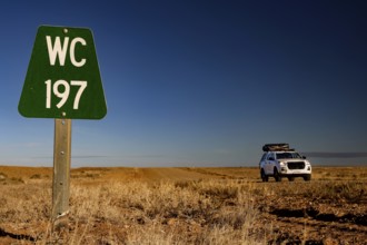 A car and a green sign along a dusty road in the desert, zero