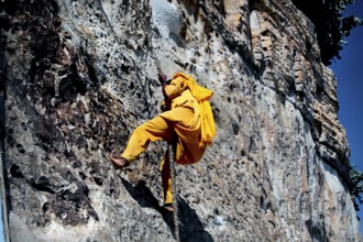 Monk dressed in yellow climbing a cliff with the help of a rope, Debre Damo, Tigray, Ethiopia