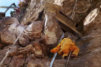 A monk climbs a rope to the entrance on rocky ground, Debre Damo, Tigray, Ethiopia