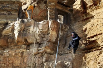 A monk climbs a rope to a monastery entrance on rocky terrain, Debre Damo, Tigray, Ethiopia