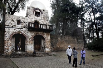 Stone gate building with arched windows and people surrounded by trees