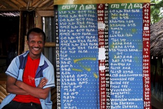A laughing man stands next to a handwritten menu in the restaurant, Konso, null