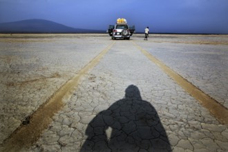 Person casting shadows in desert landscape in front of a land cruiser, Kusrawad, Ethiopia