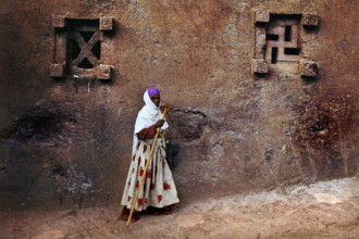 Woman in colorful clothes leaning against a decorated church wall, Lalibela, Amhara, Ethiopia