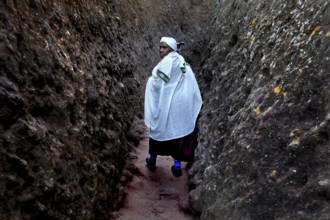 A person wearing traditional clothing walks through a narrow rocky passage near Bete Gyorgis,