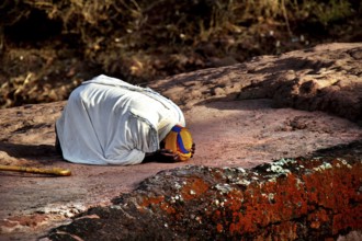 Kneeling person praying on rock, expressing deep faith near Bete Gyorgis, Lalibela, Amhara,