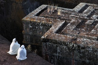 Historic rock church of Bete Gyorgis in Lalibela with two believers in traditional clothing,