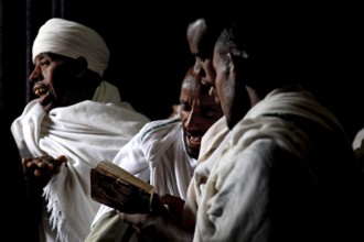 Men read Bete Gabriel and Raphael in the dark church, engrossed in prayer, Lalibela, Amhara,