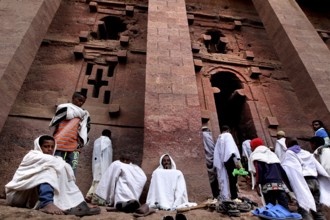 Pilgrims wearing white cloaks gather solemnly in front of the Bete Medhane Alem rock church at