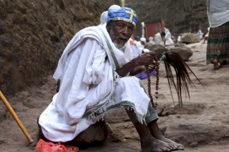 A praying monk in traditional clothing on a stone path, Lalibela, Amhara, Ethiopia