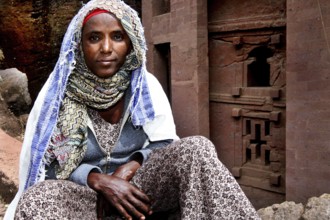 A woman sits thoughtfully in front of a traditional building, Lalibela, Amhara, Ethiopia