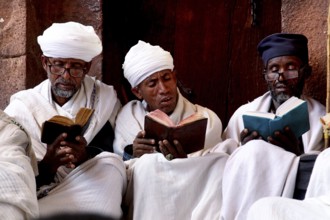 Three men in traditional clothes read books together, Lalibela, Amhara, Ethiopia