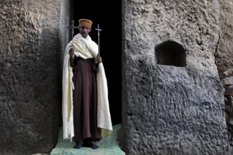 Priest with crosses standing in stone niche, Lalibela, Lasta Mountains, Ethiopia