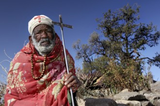Abbe Adamu holds a cross in the harsh, natural environment of the Lasta Mountains, Lalibela,
