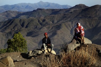 Two people sit in front of the impressive mountain scenery of the Lasta Mountains, Lalibela,