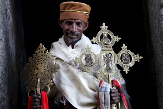 Priest with decorative crosses in traditional robes against dark background, Lalibela, Lasta