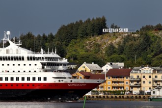 Hurtigruten ship off the coast of Kristiansund with colorful houses and forest, Kristiansund, Møre