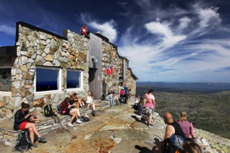 Stone hut on a summit plateau with visitors enjoying the view, Hardangervidda, Gausdal, Norway