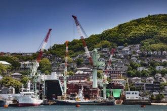 Nagasaki harbor with shipyard and cranes in front of wooded hill and city view, Nagasaki, Japan