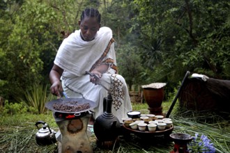 Woman in traditional dress preparing coffee during a ceremony in a natural setting, Yirga Alem,