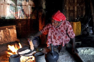 Woman wearing red clothes bakes traditional food in a hut over an open fire, Yirga Alem, Ethiopia