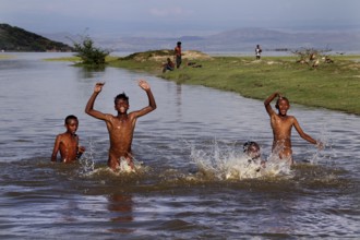 Children play happily in water on the shore of a lake, surrounded by nature, Ziway, Ethiopia
