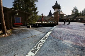 Arctic circle marking on cobblestones in front of picturesque buildings, Napapiiri, Finland