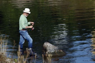 Angler with hat standing in water at a calm lake, Suomenlinna, Helsinki, Finland
