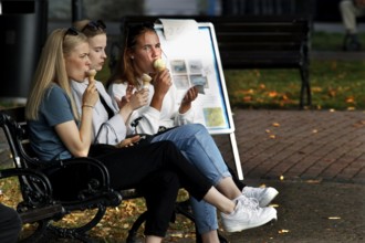 Women enjoying ice cream on a bench in autumnal Naantali, Naantali, Finland