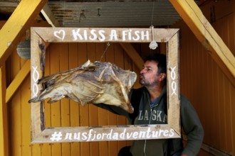 Man posing with stockfish in wooden frame in Nusfjord, Nusfjord, Flakstadøy, Norway