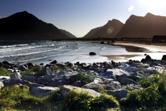Sunny beach with views of mountains and calm waves surrounded by picturesque rocks, Flakstad,