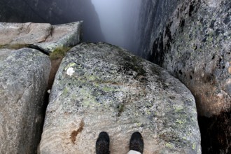 Two feet stand on a rock looking into the depths of Kjeragbolten, Lysefjord, Rogaland, Norway