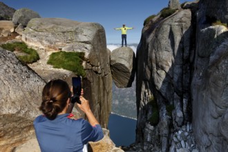 Tourist is photographed by another person while balancing on Kjeragbolten, Lysefjord, Norway