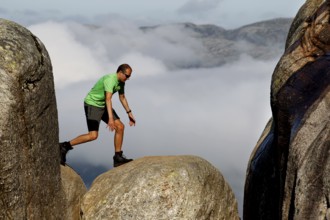 Tourist balancing on Kjeragbolten between rocks high above the clouds, Lysefjord, Norway