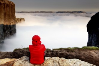 Person in red enjoying the spectacular view over a cloud-covered fjord valley, Lysefjord, Norway