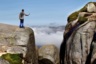 Tourist taking a selfie on cliffs near Kjeragbolten with clouds in the background, Lysefjord,