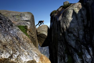 Tourist balancing on Kjeragbolten between imposing cliffs under blue sky, Lysefjord, Rogaland,