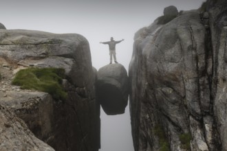 Person standing on Kjeragbolten rock hanging in the air, Lysefjord, Rogaland, Norway